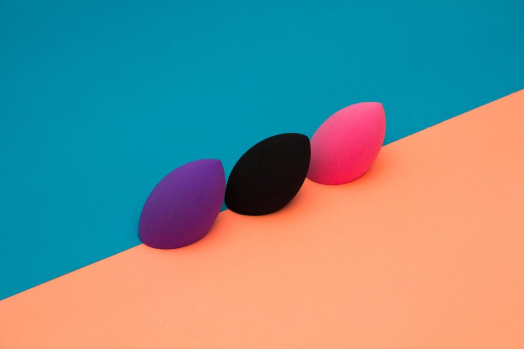 Three makeup sponges on a vibrant, split-color background create a striking minimalist composition.