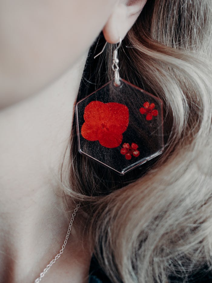 Close-up of a stylish resin earring with embedded red floral designs worn by a woman.