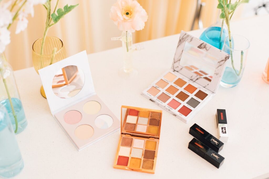 Aesthetic display of makeup palettes and lipsticks surrounded by flowers.